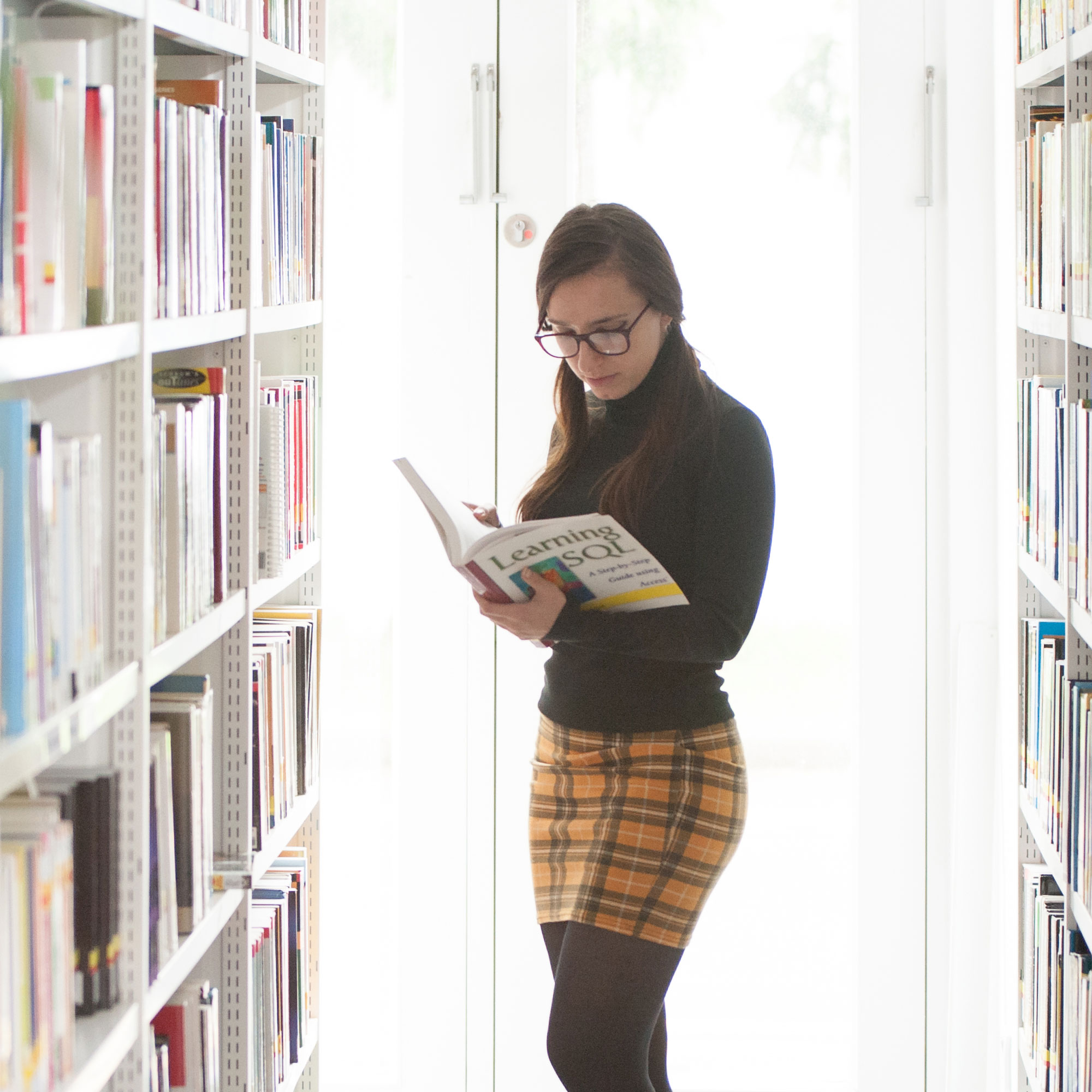 Girl with glasses on stood reading book in library