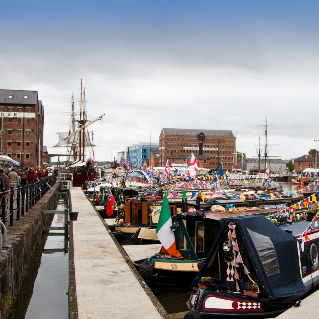 View of Gloucester Docks with canal boats adorned with colourful bunting and tall ships.