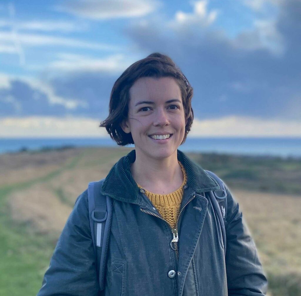 Head and shoulders photo of Pippa standing on land overlooking the sea.