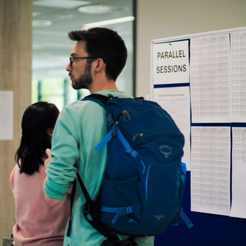 Student wearing a rucksack walking past a 'Parallel Sessions' sign board.