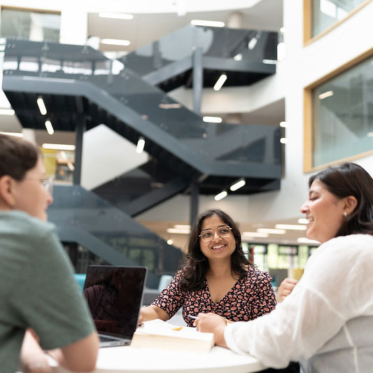 Students sit at a table in the atrium at Oxstalls campus.