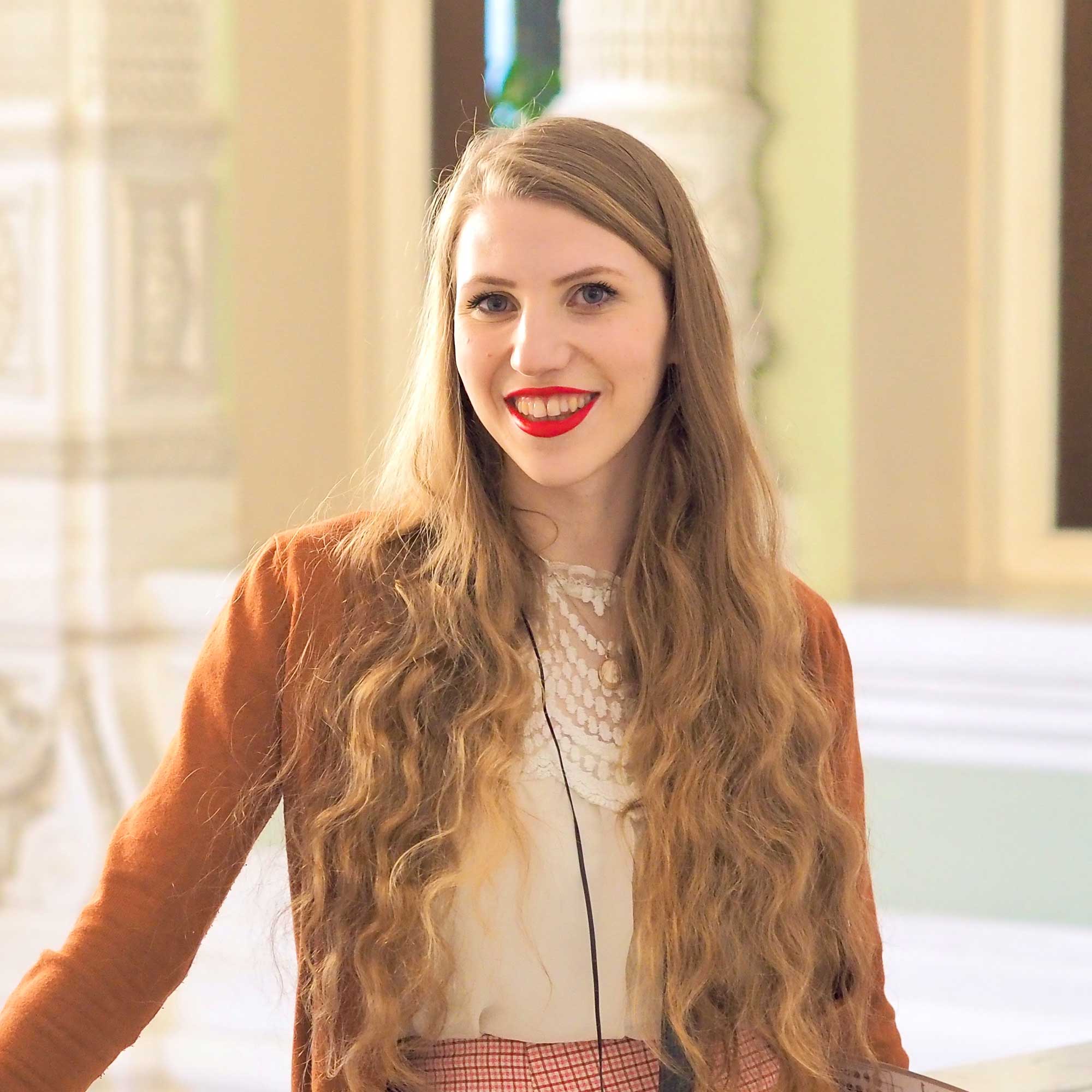 Antonia Miejluk smiling in an orange cardigan with light green walls and cream pillars in the background