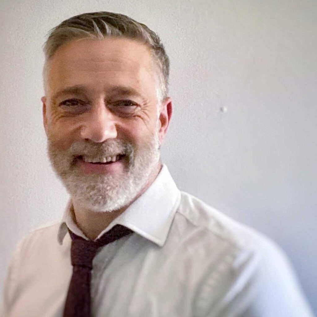 Head and shoulders portrait shot of David Webster wearing a shirt and tie.